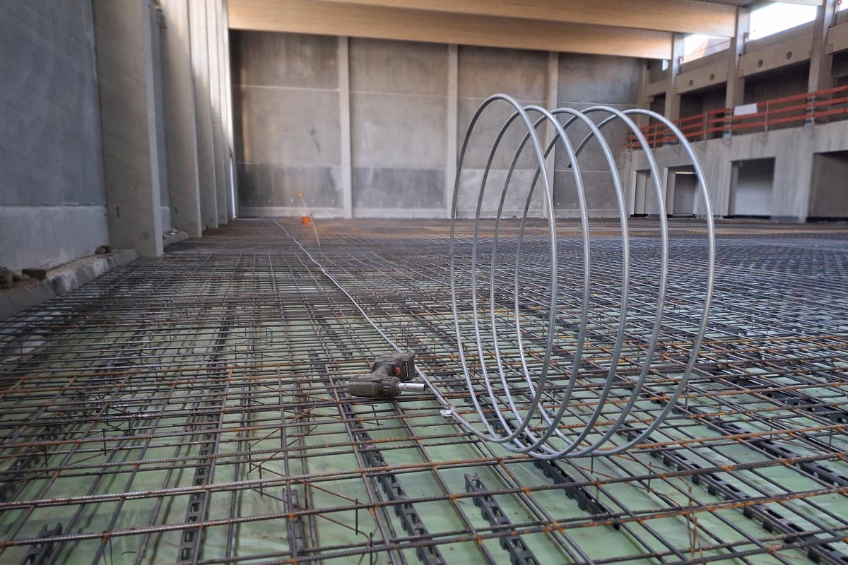 Vorbereitung für den Potentialausgleich: Ein Coil Erdungsdraht, eine Verbindungsklemme und ein Elektrowerkzeug auf der Bewehrung vor dem Betonguss in einer großen Industriehalle.